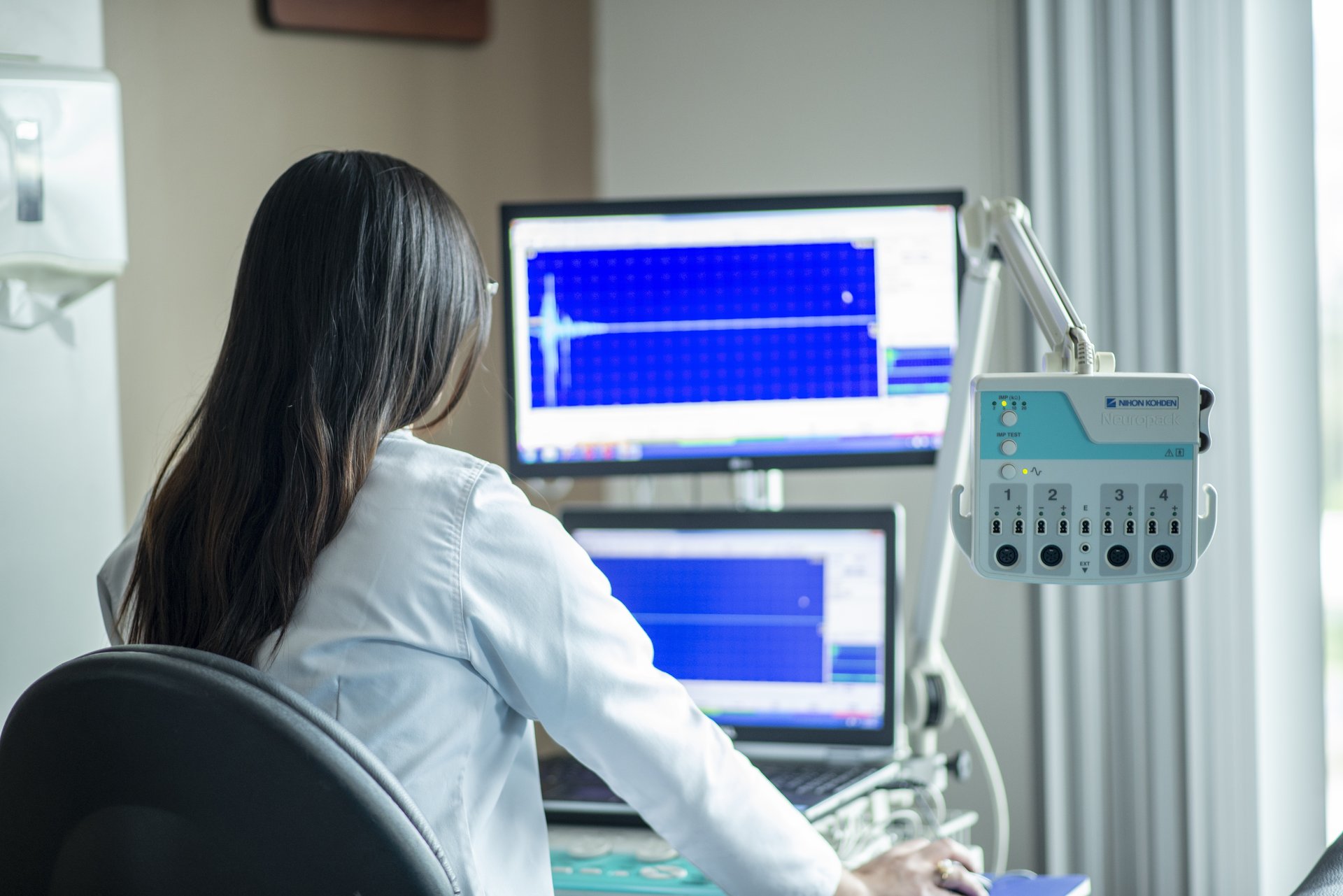 Clinician at a clinic desk reviewing patient data on a laptop.